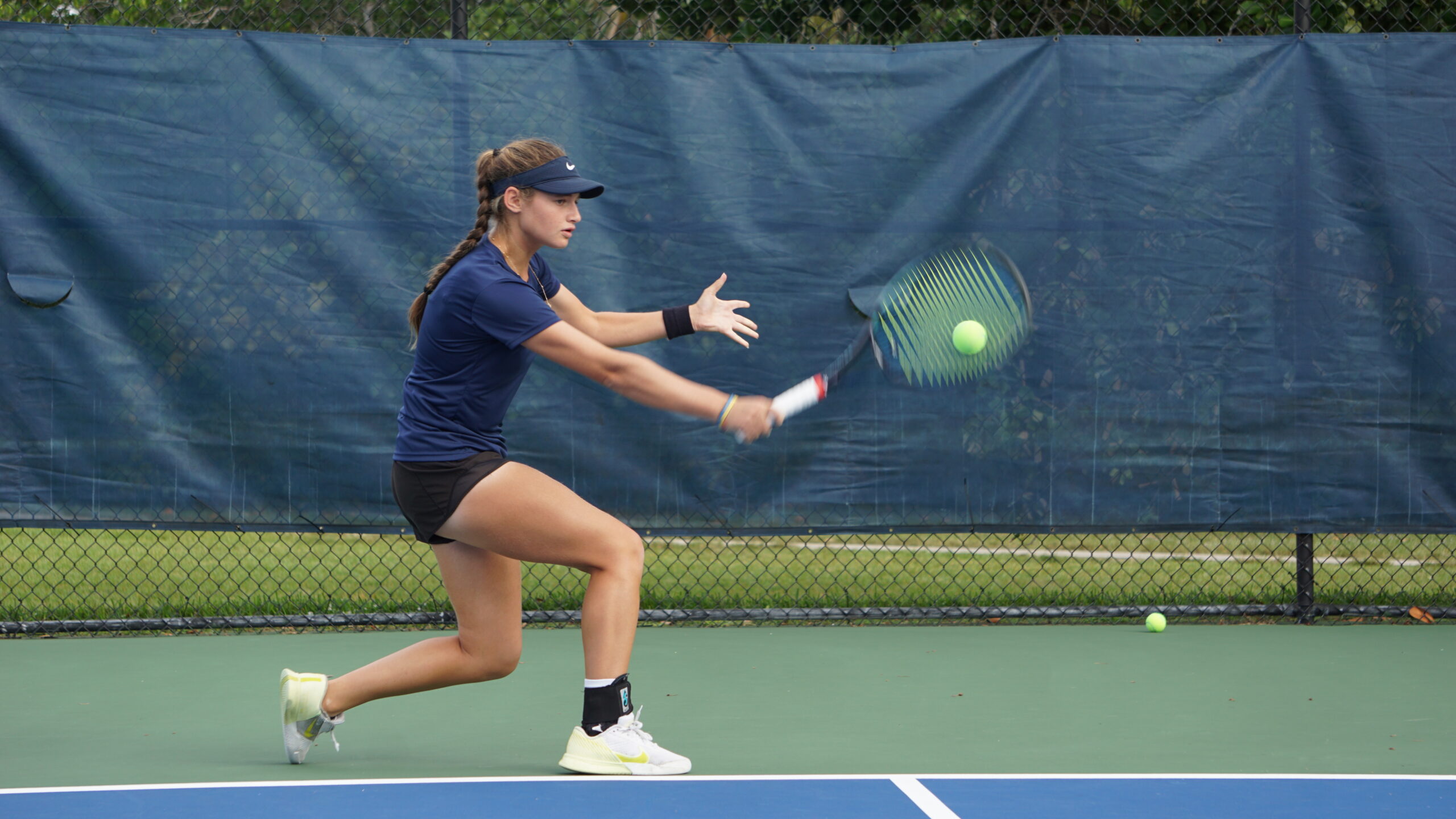 NMBA junior tennis player hitting backhand slice wide shot North Miami Beach Academy